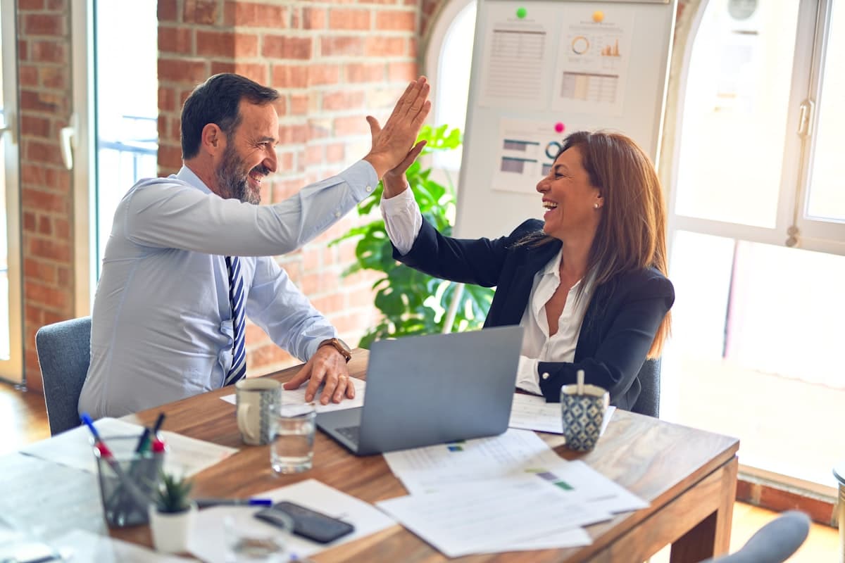 Two colleagues celebrating a deal over a laptop at a brick-walled office